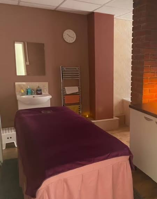 A softly-lit treatment room with a massage bed, fresh towels and warm lighting