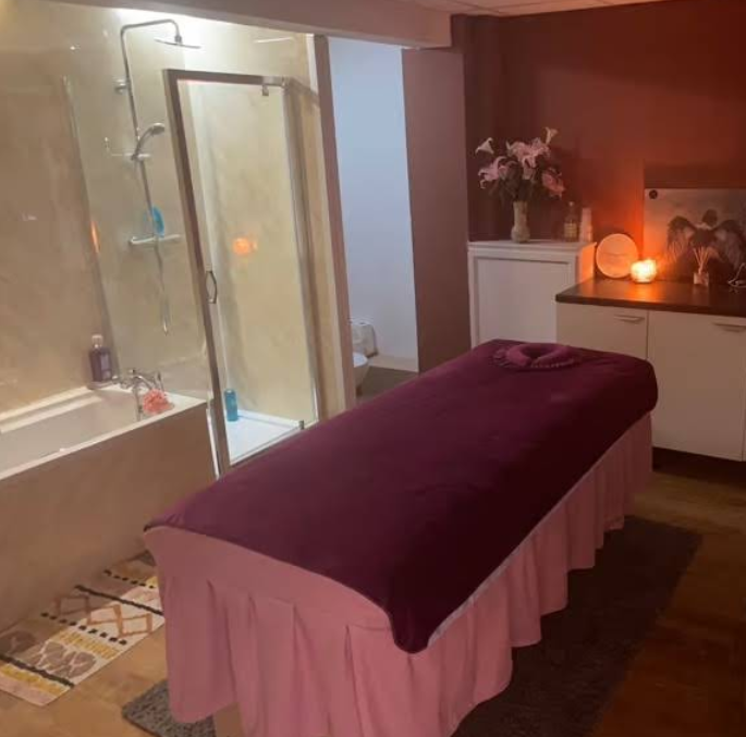 A private treatment room with a massage bed, shower, fresh flowers and candlelight